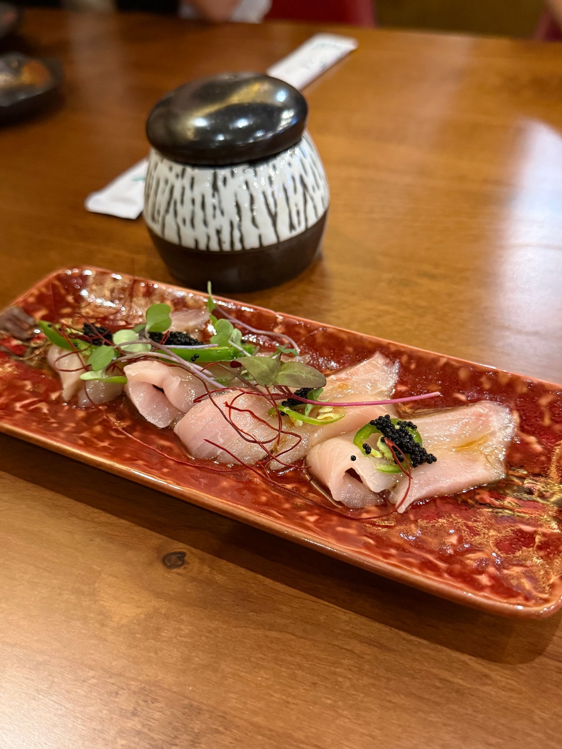 Long rectangular plate with sliced meat and garnish on a wooden table in a restaurant