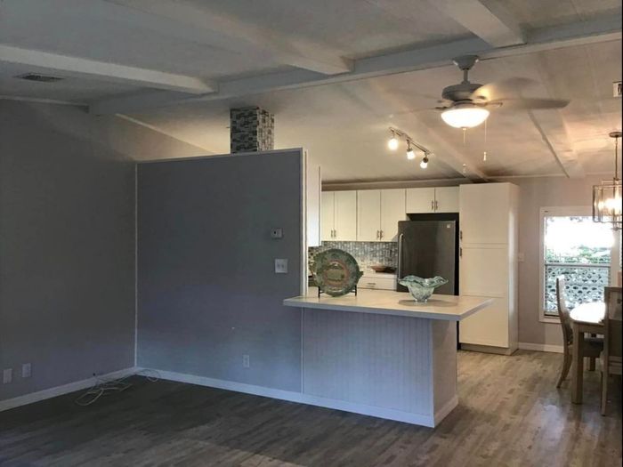 A living room with a ceiling fan and a kitchen in the background.