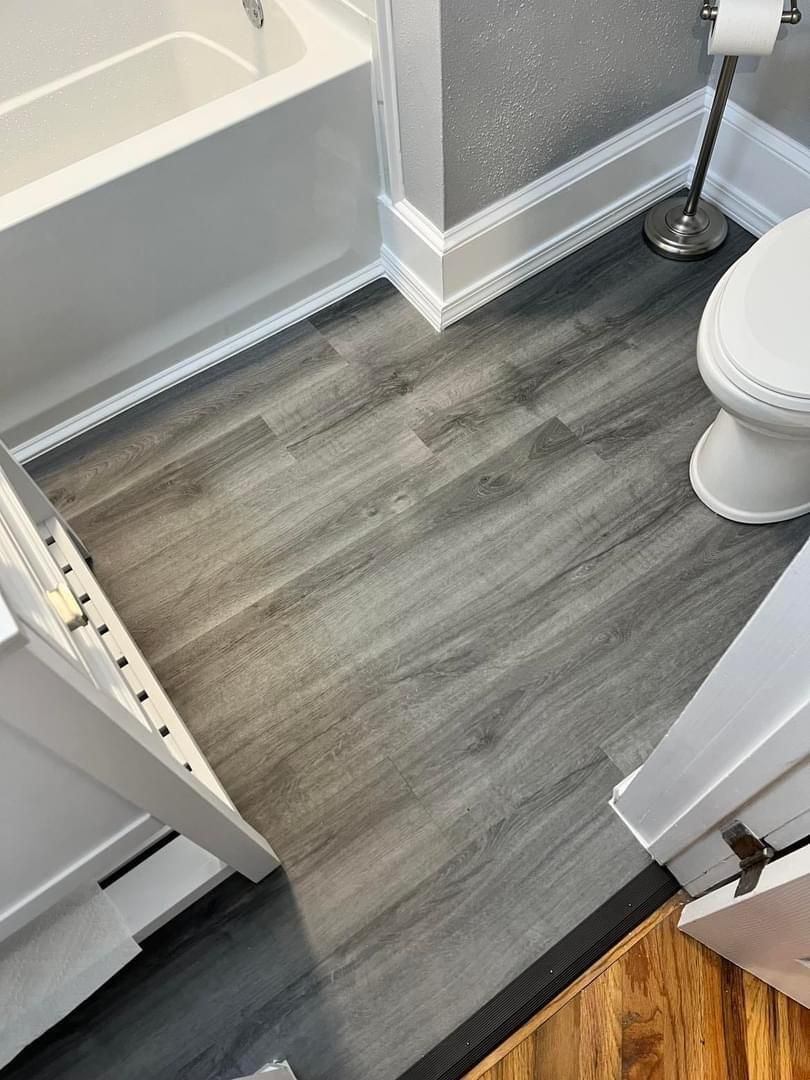 A bathroom with a toilet , bathtub , and wooden floor.