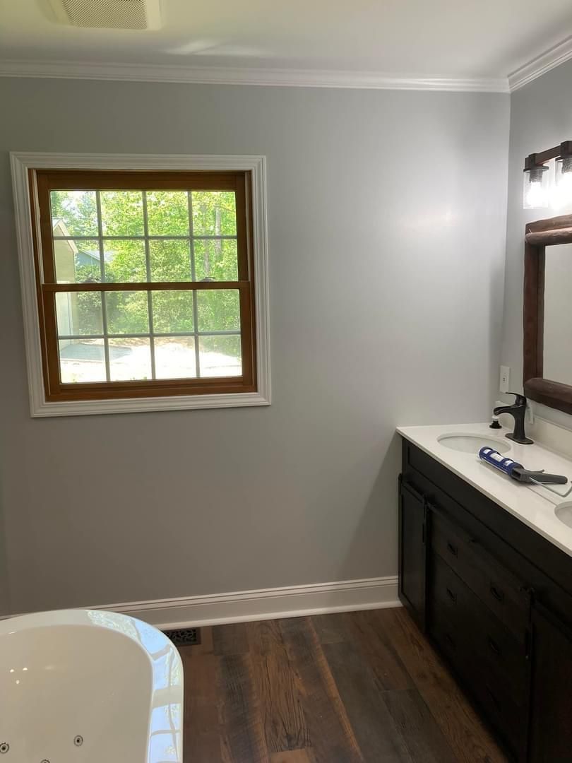 A bathroom with a tub , sink , mirror and window.