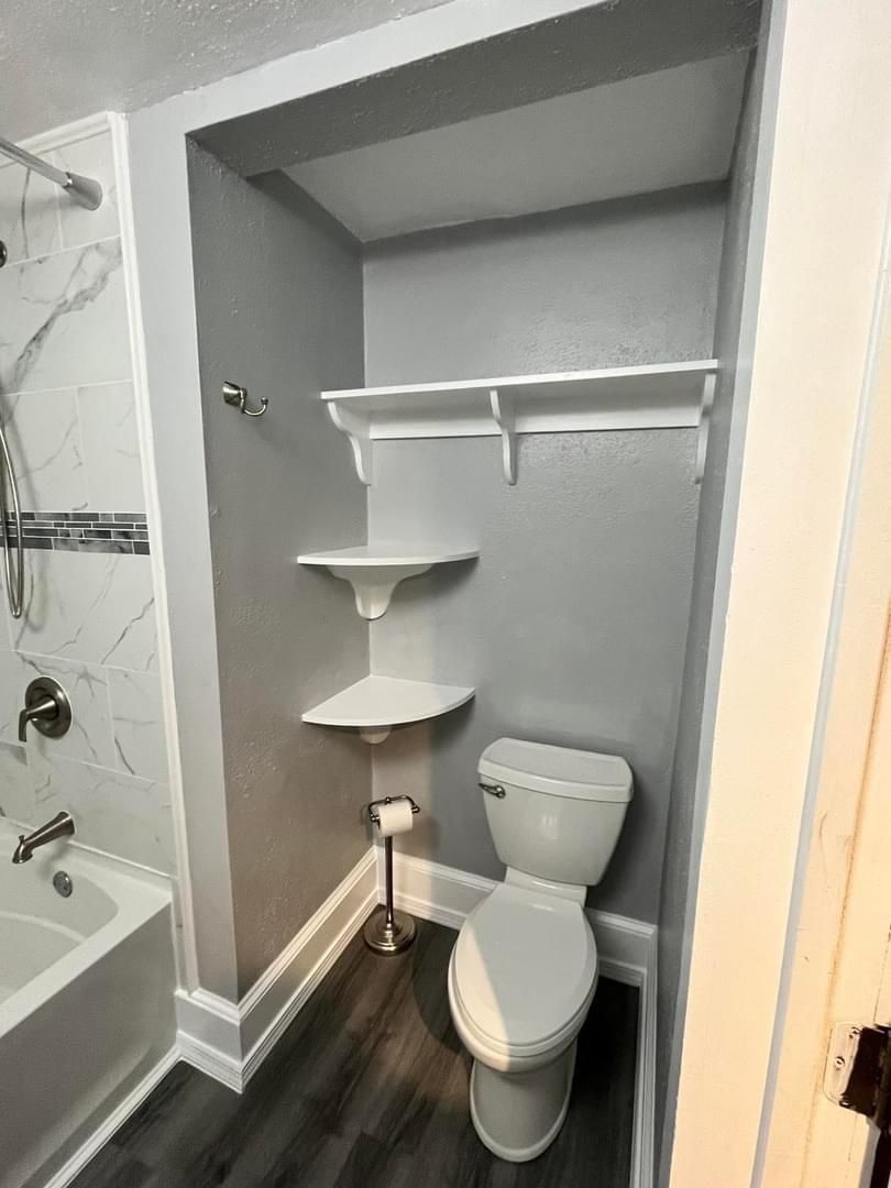 A bathroom with a toilet , tub , shower and shelves.
