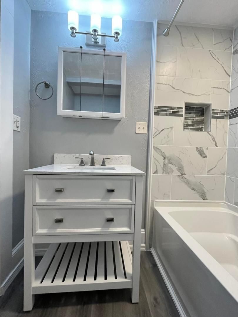 A bathroom with a sink , mirror and bathtub.