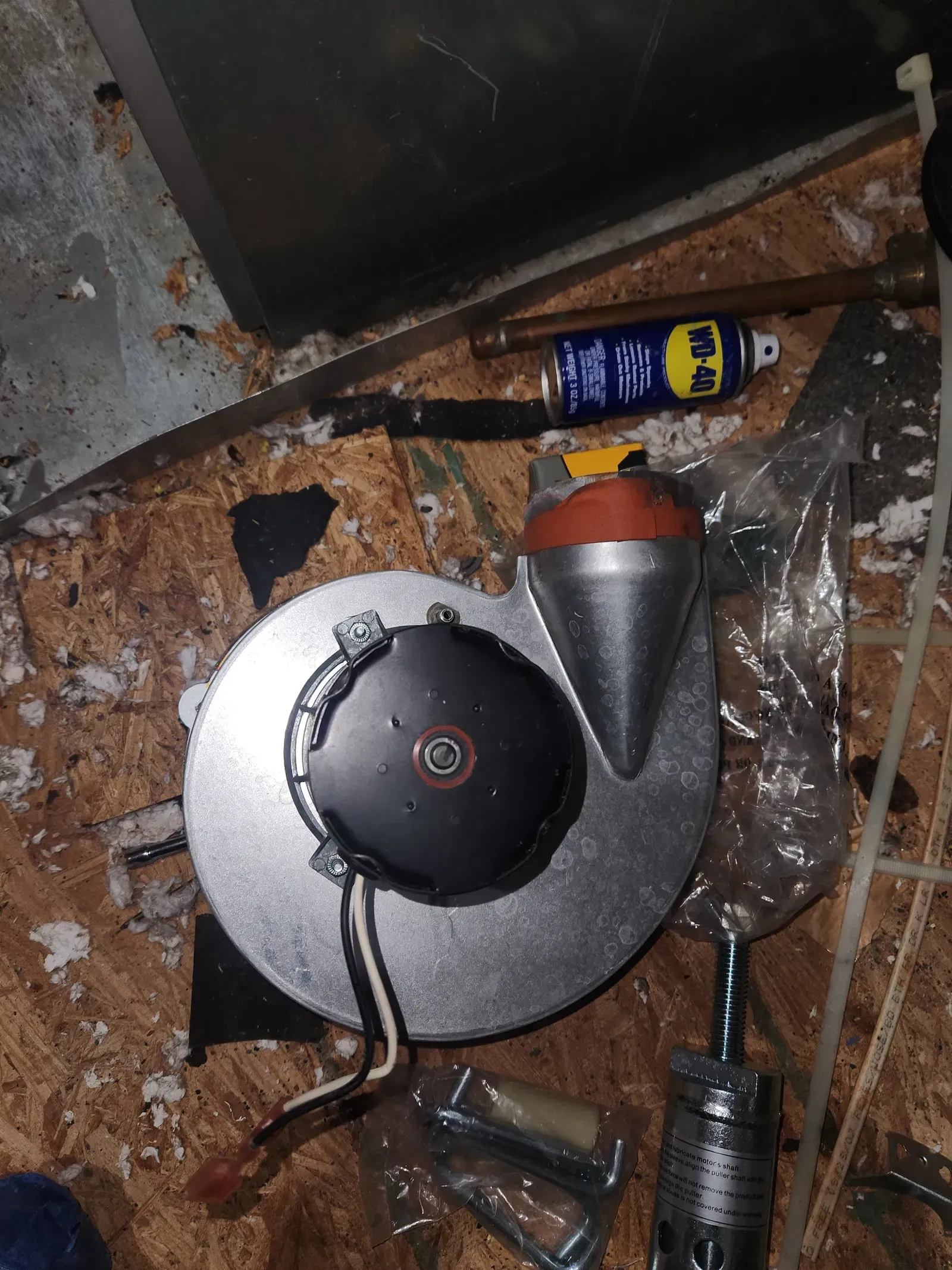 A blower motor with wiring and a can of WD-40 on a wooden surface.