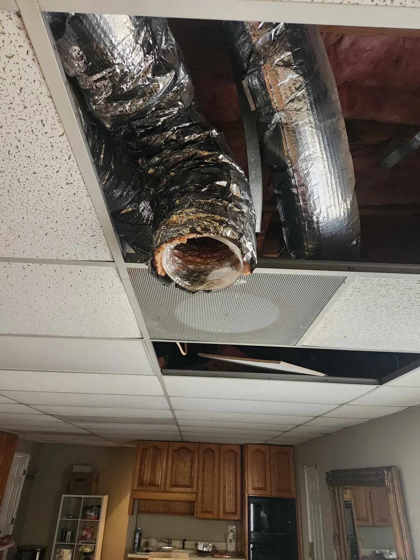 Ceiling damage reveals HVAC ductwork. Damaged ceiling tiles and exposed ducting. Interior shot with cabinetry below.