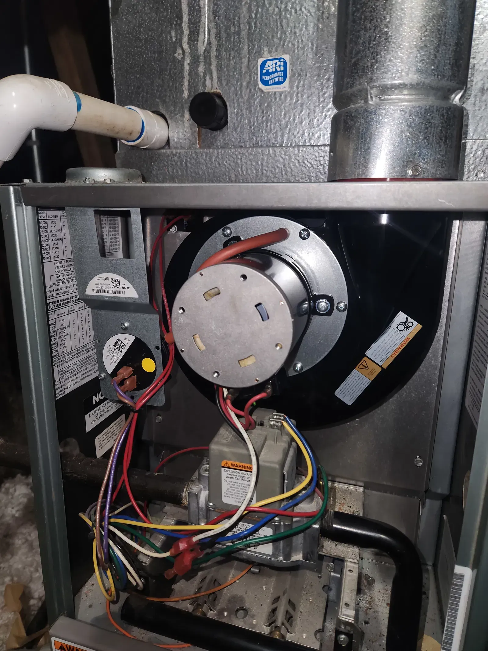 Furnace interior, showing fan, wires, and components. Silver and black with various colored wires.