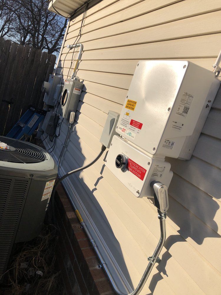 Solar panel inverter and electrical components mounted on a beige siding wall near an AC unit.
