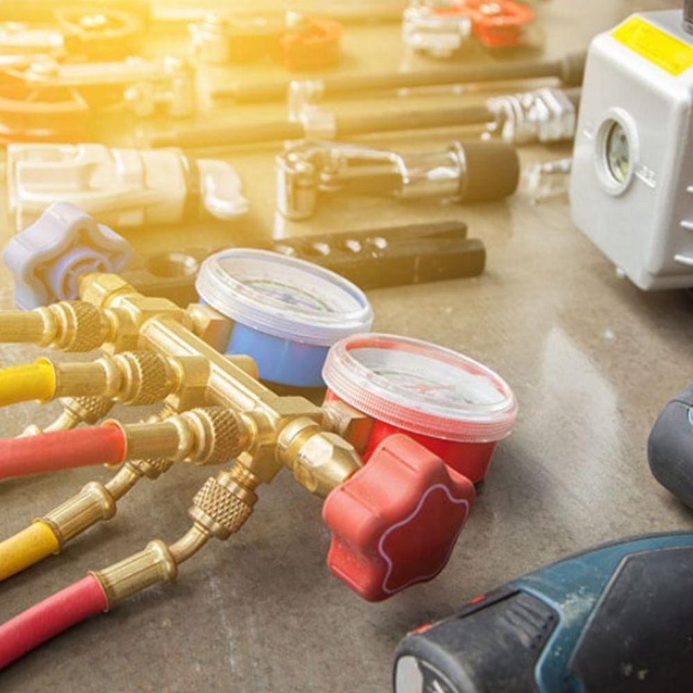 HVAC tools: gauge manifold with hoses, other tools, and a vacuum pump on a concrete surface.