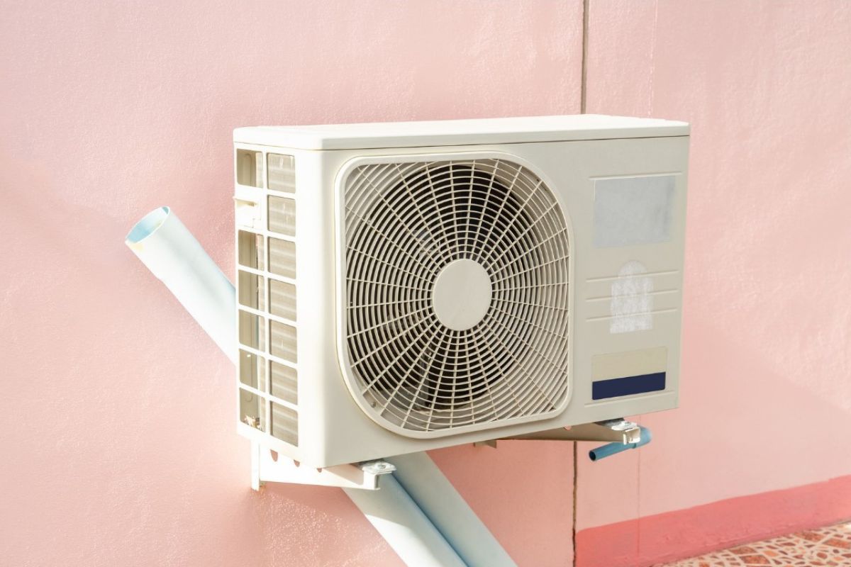 Air conditioning unit mounted on a pink wall; blue insulated pipes visible.