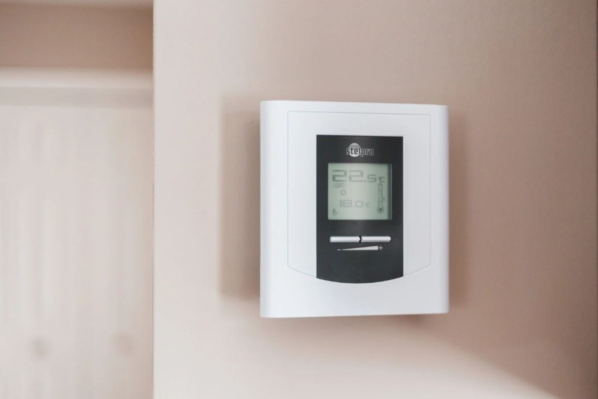 White thermostat mounted on a light beige wall. The display shows numbers and symbols.