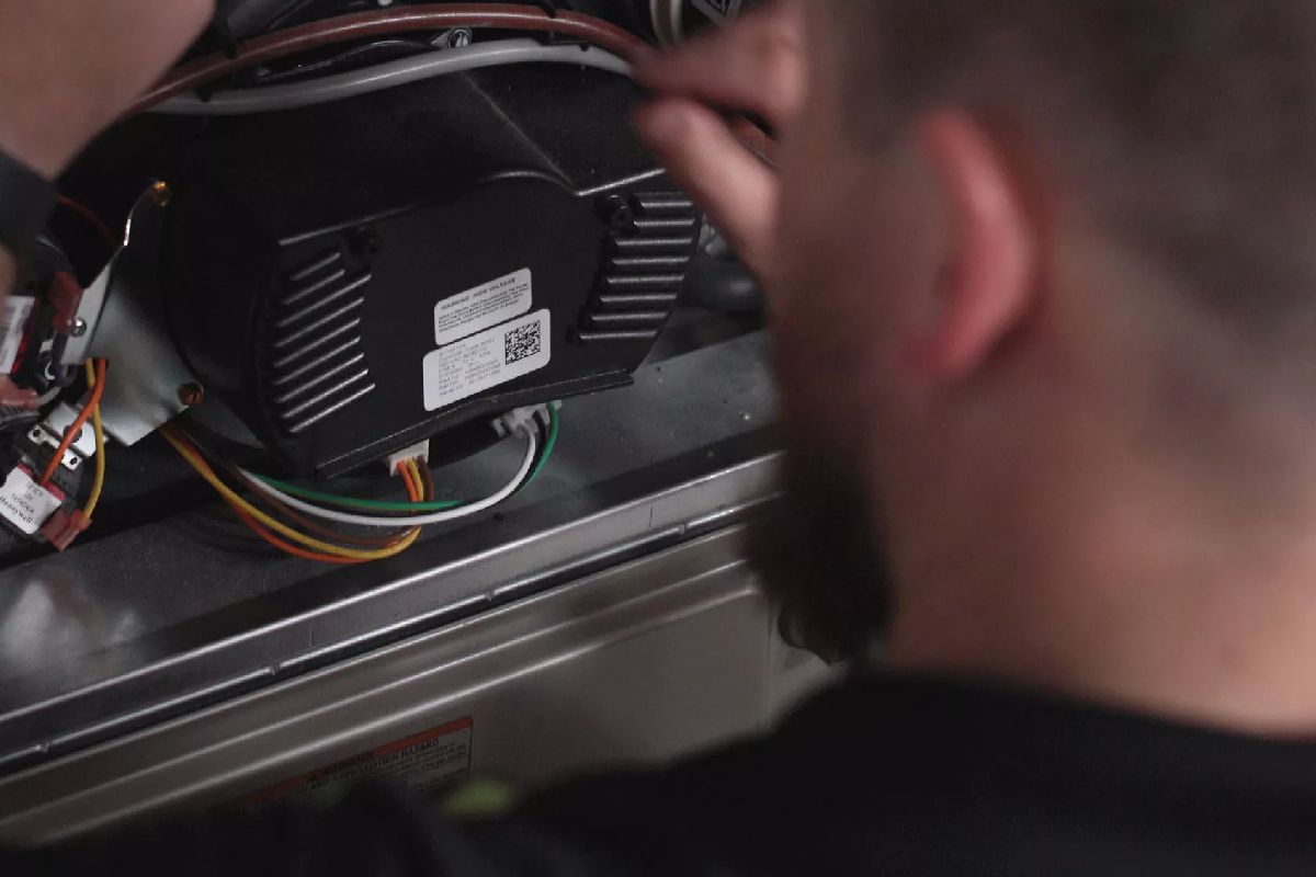 A technician working on HVAC equipment, examining a black control box.