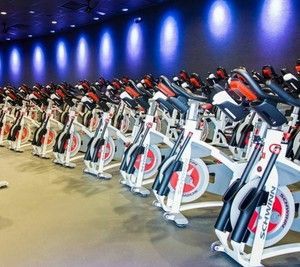 Rows of stationary bikes in a spin class studio with blue lighting on the wall.