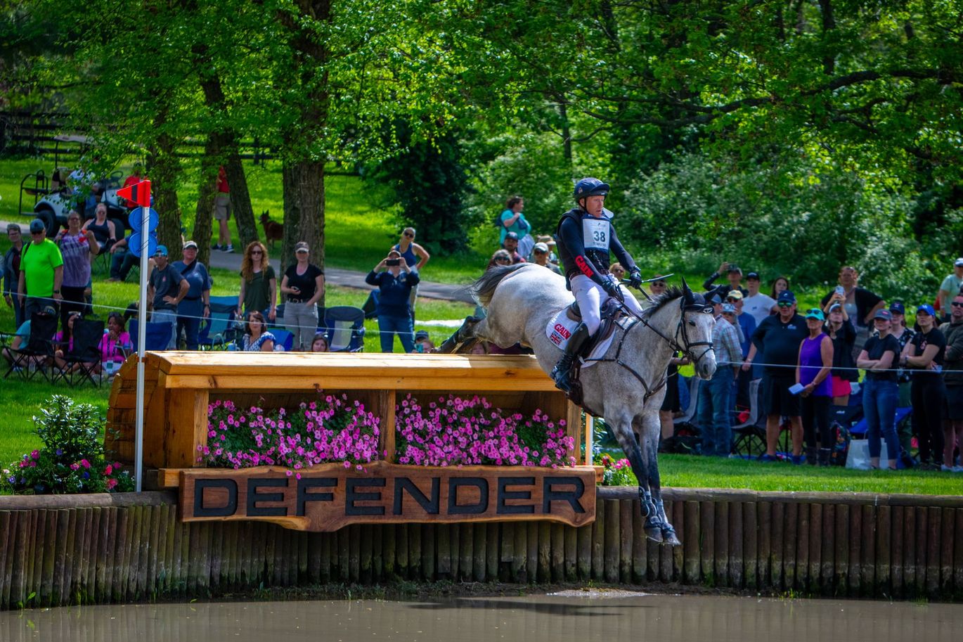 A woman is riding a horse over a wooden sign that says defender.