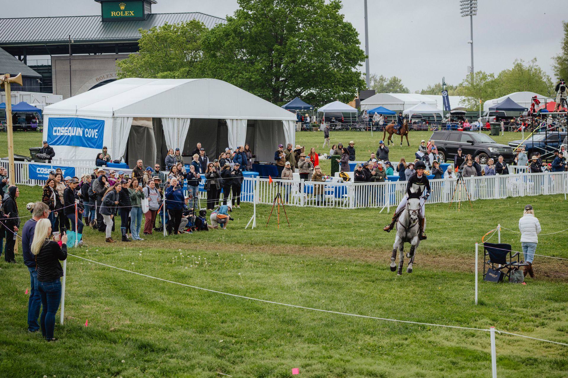 A woman on a horse rides in front of a crowd standing near a tent