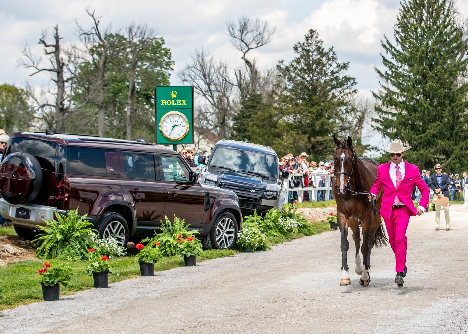 A man in a pink suit is leading a horse down a road.