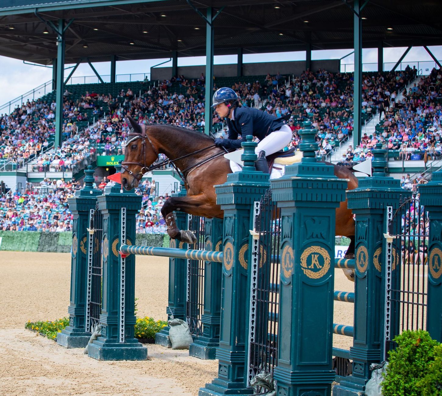 A woman is riding a brown horse over a fence.