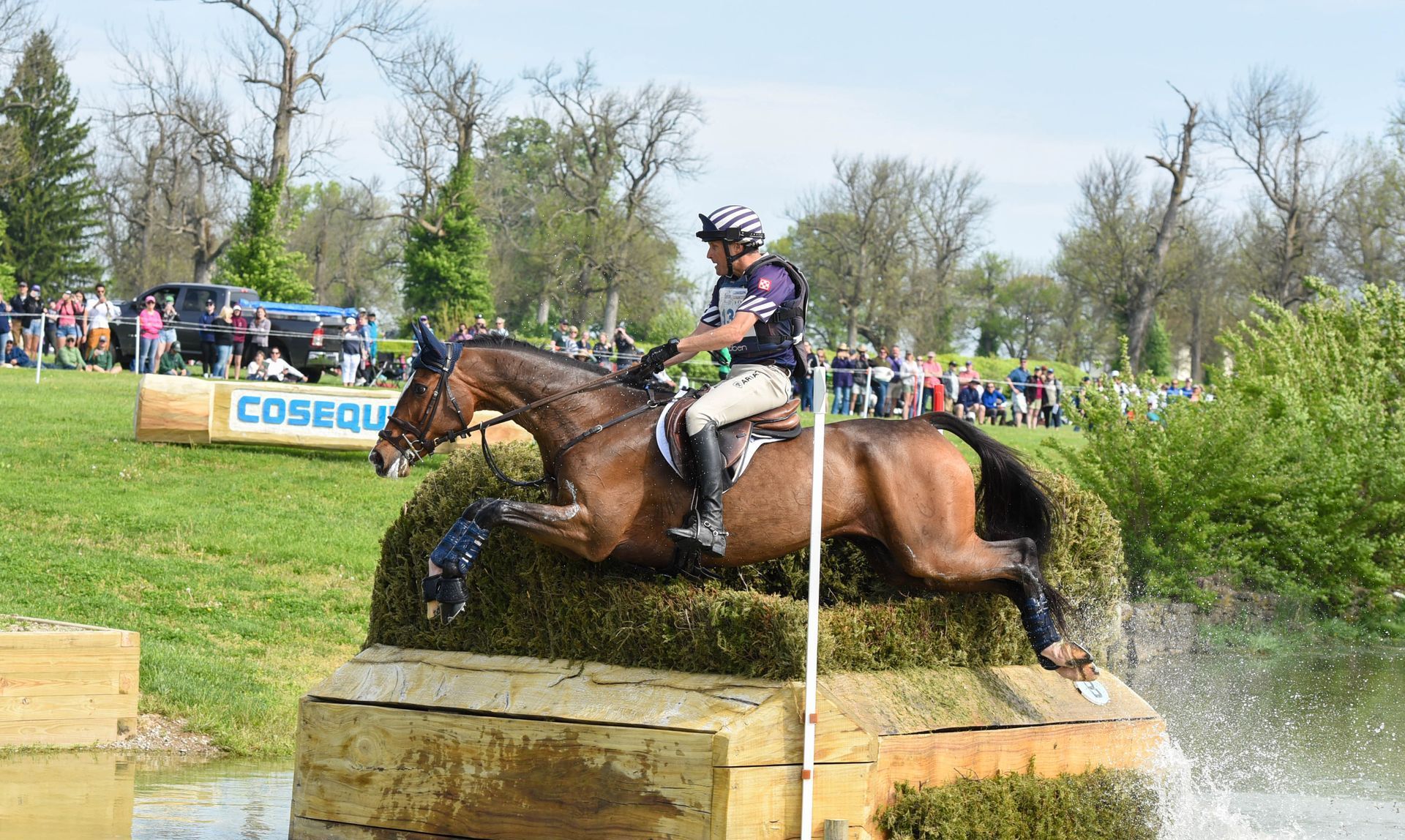 A man is riding a horse over a wooden block in the water.