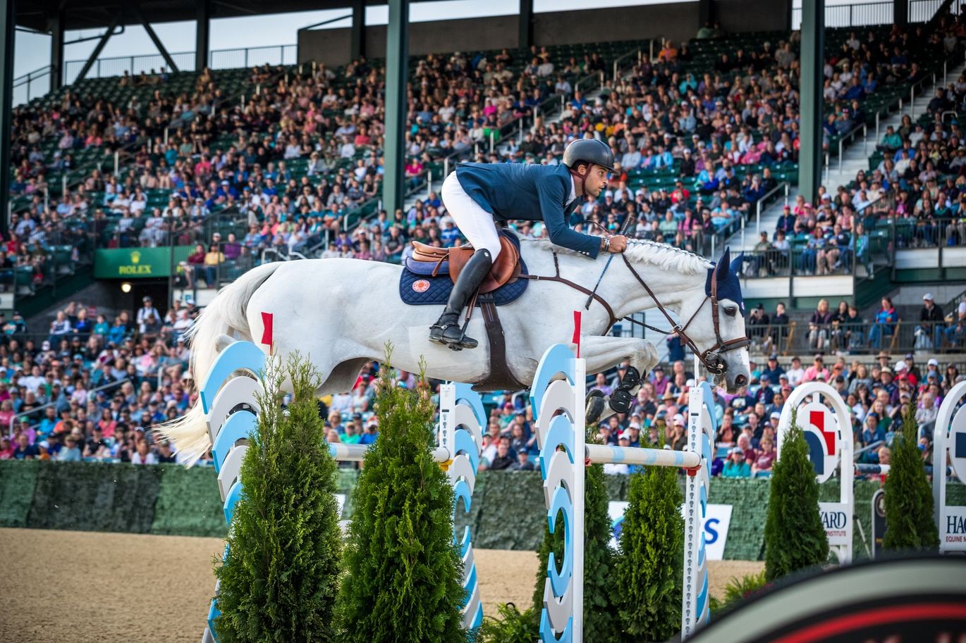 A man is riding a white horse over a jump.