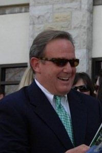 A man in a suit and tie is wearing sunglasses and smiling.