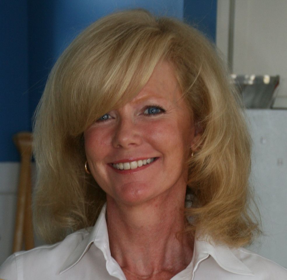 A woman with blonde hair is smiling and wearing a white shirt.
