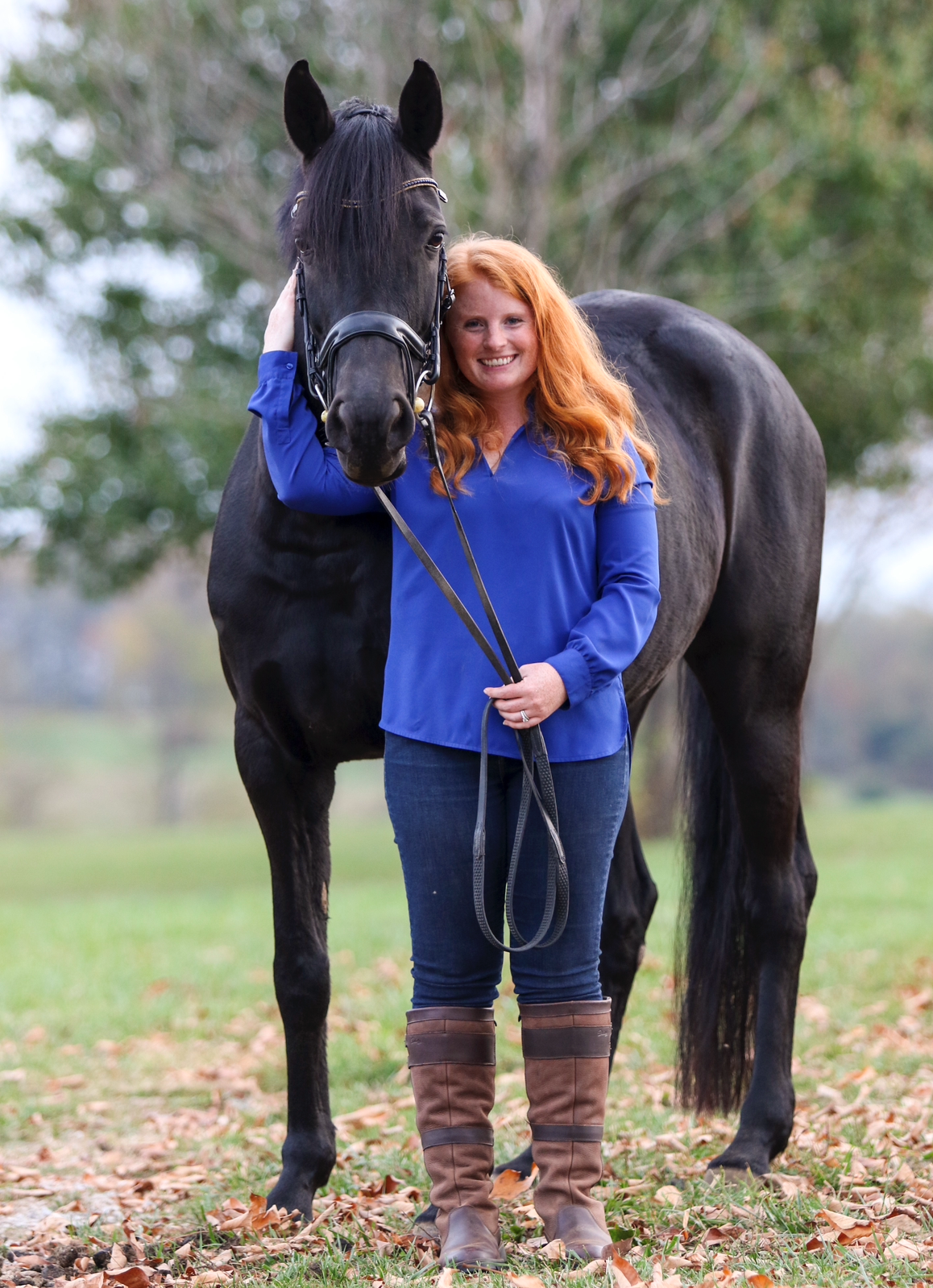 A woman in a blue shirt is standing next to a black horse.