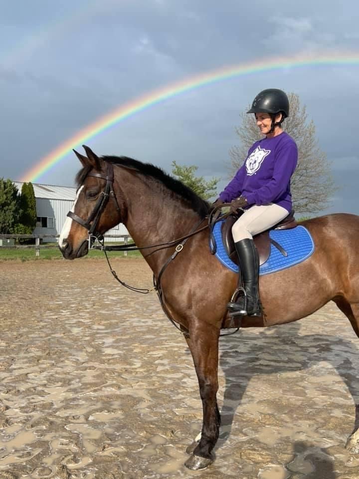 A woman is riding a horse under a rainbow.