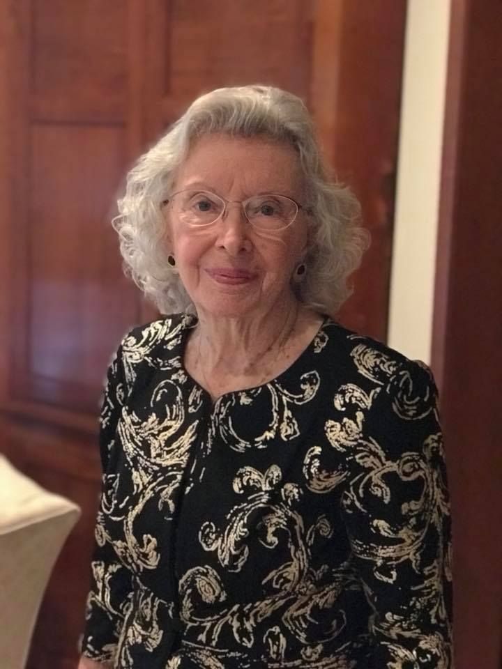 An elderly woman wearing glasses and a black and gold dress