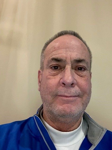 A man with a beard is wearing a blue jacket and a white turtleneck.