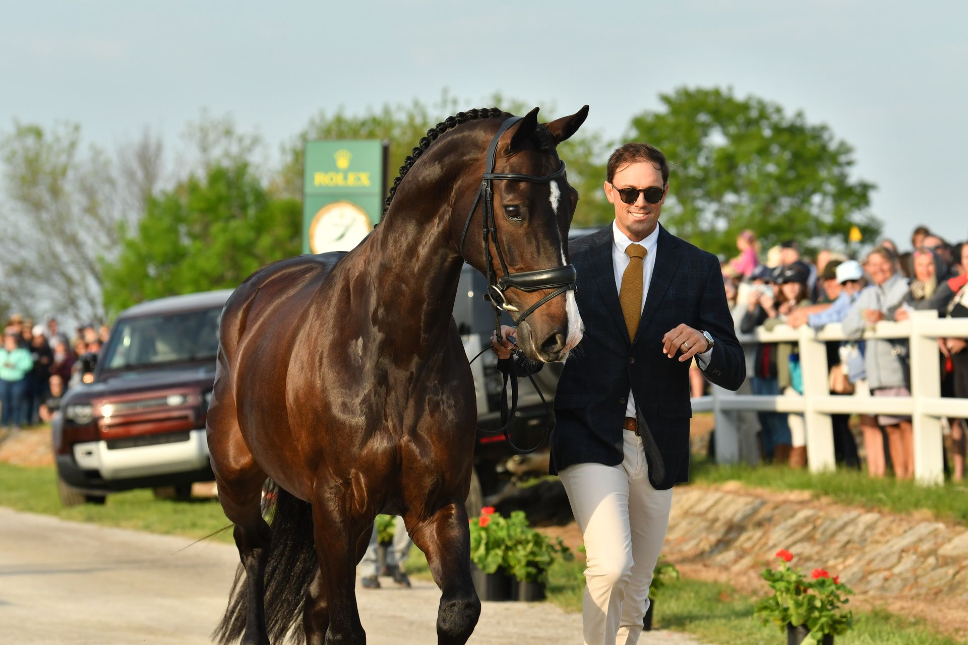 A man in a suit and tie is walking a brown horse.