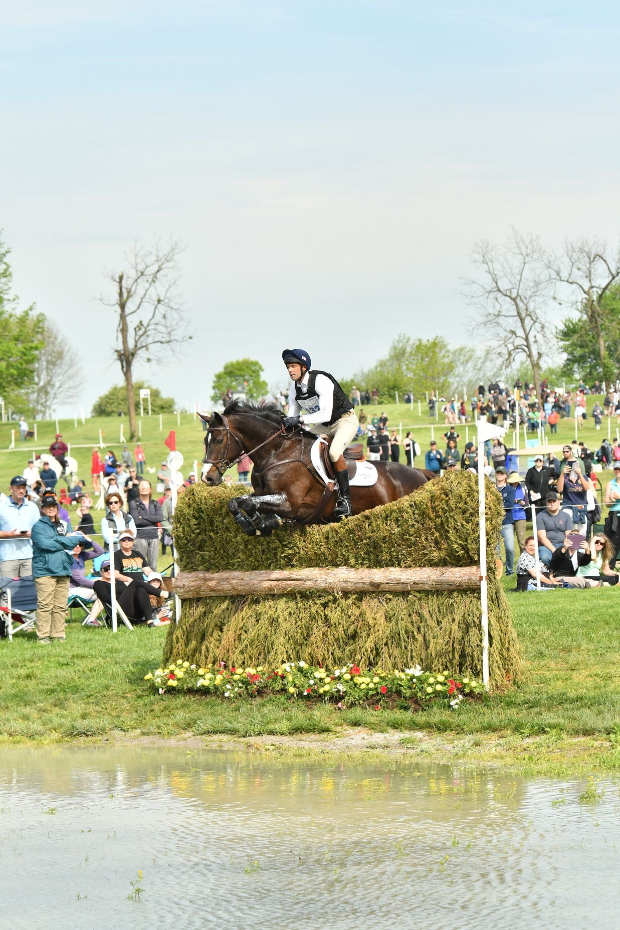 A person is riding a horse over a hay bale in a field.