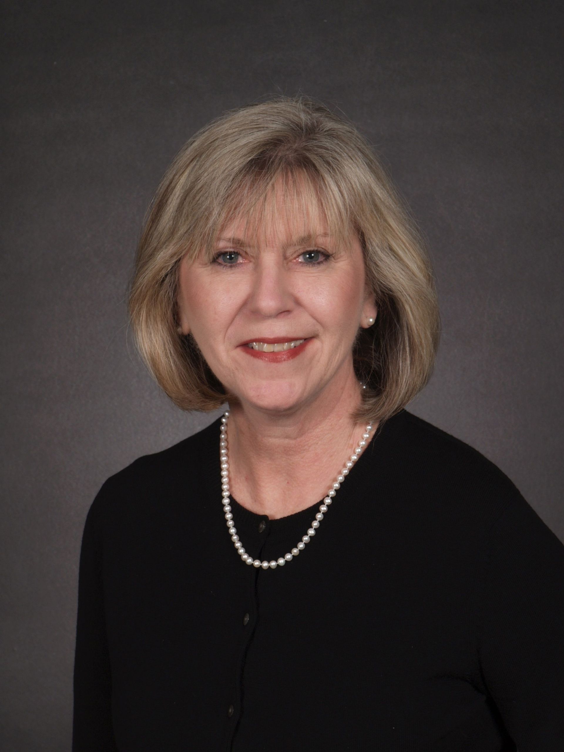 A woman wearing a black shirt and a pearl necklace is smiling for the camera.