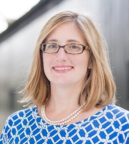 A woman wearing glasses and a pearl necklace is smiling for the camera.