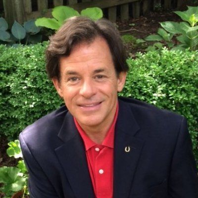 A man in a suit and red shirt with a horseshoe pin on his jacket