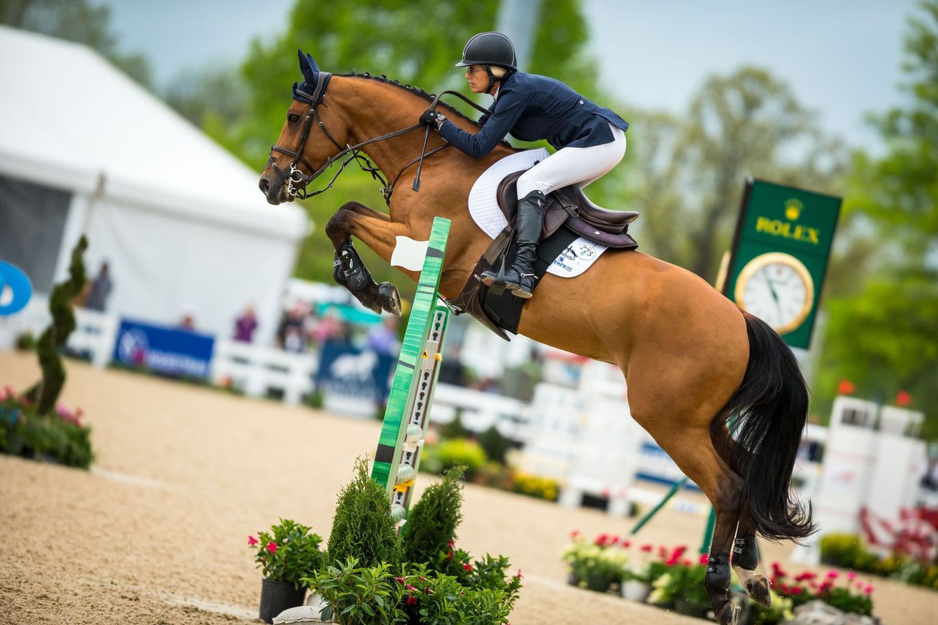 A woman is riding a brown horse over a jump.