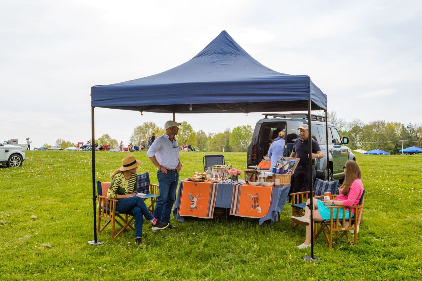 A group of people are sitting under a tent in a field.