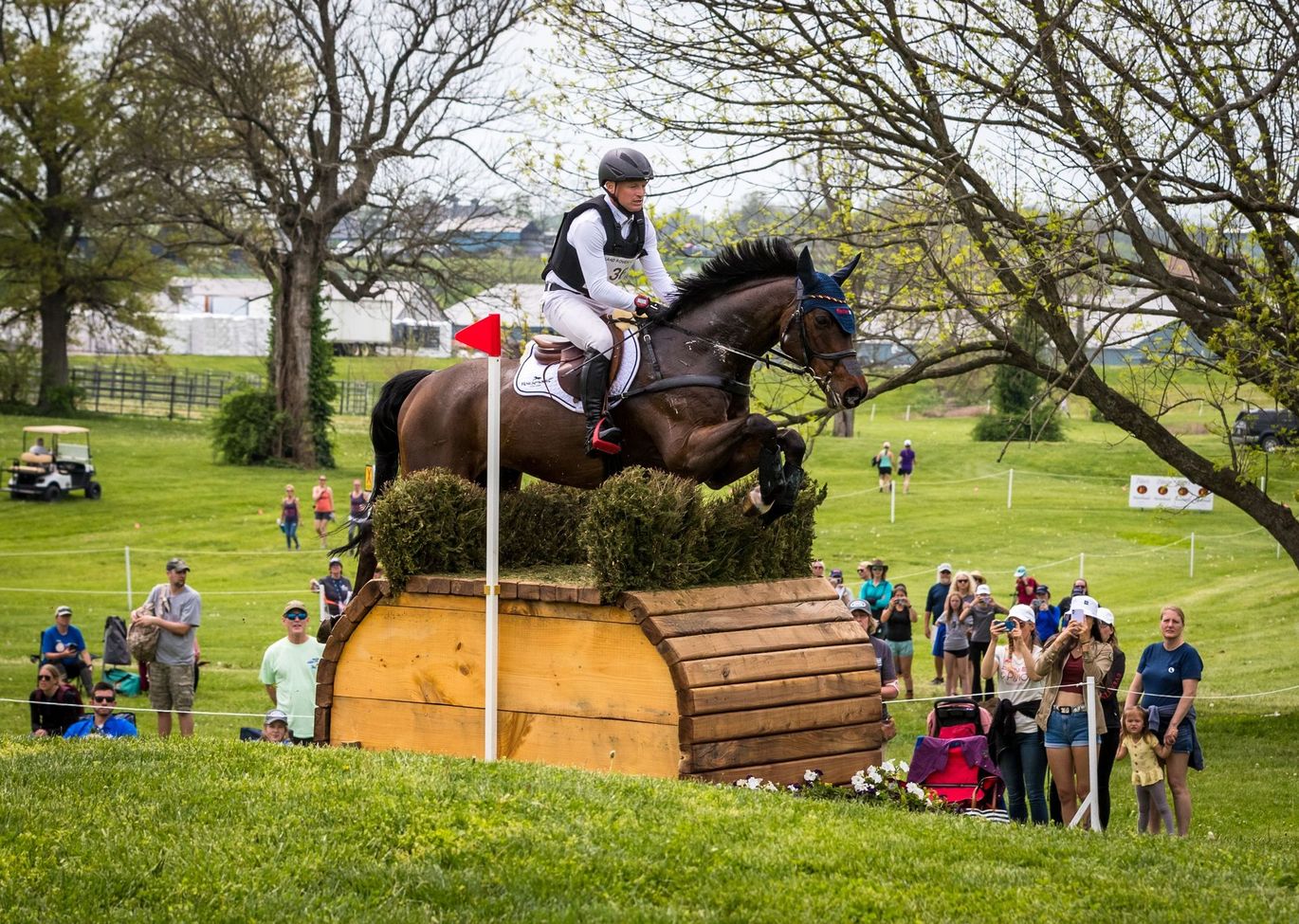 A man is riding a horse over a wooden obstacle in a field.