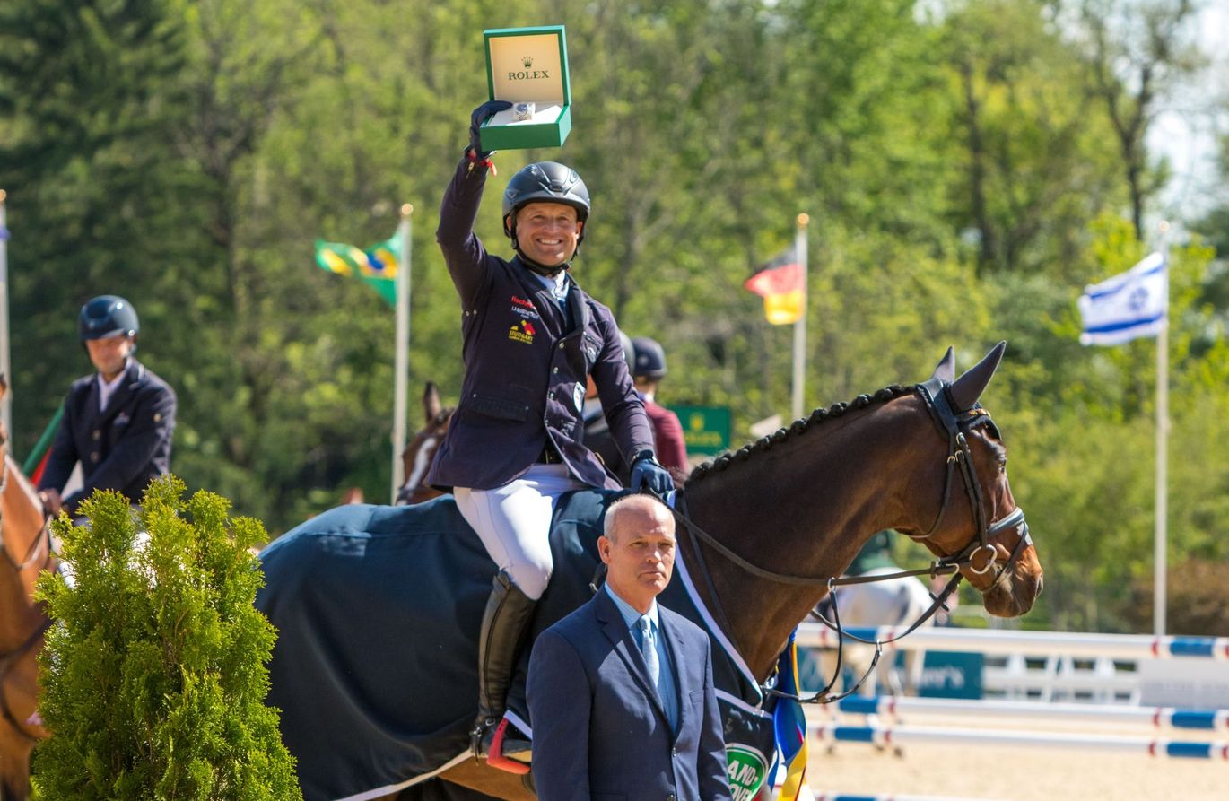 A man in a suit is standing next to a woman on a horse holding a trophy.