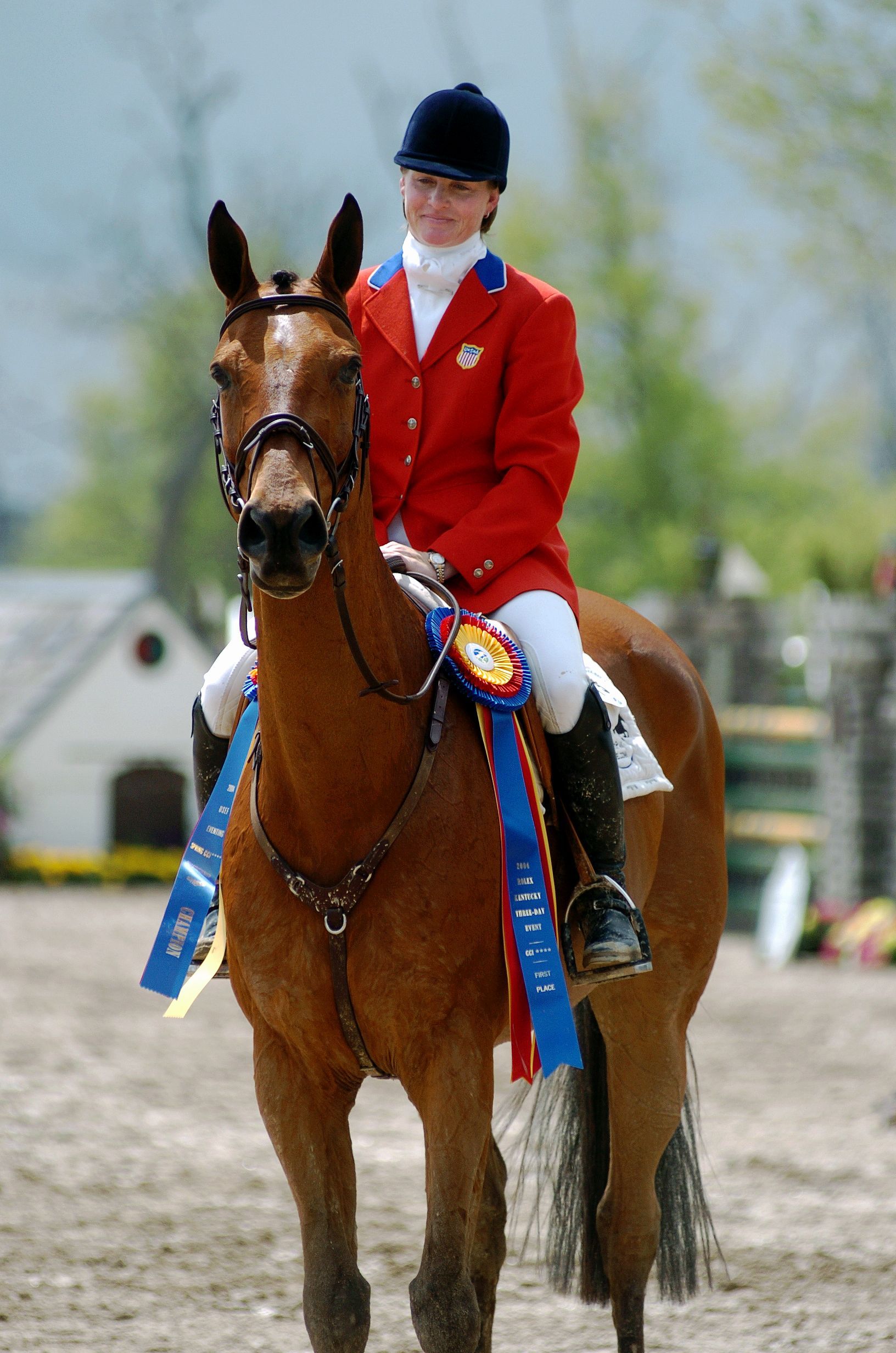 A woman in a red jacket is riding a brown horse