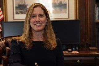 A woman is sitting at a desk in front of a computer and smiling.