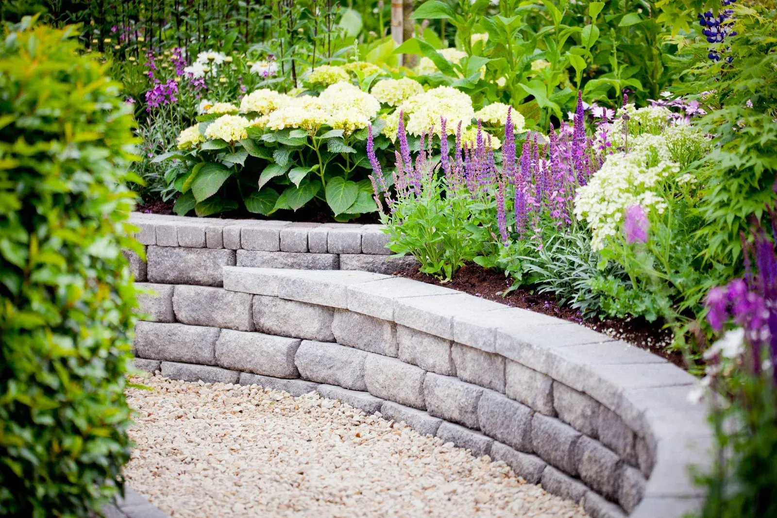 Stone retaining wall with garden beds filled with flowers and greenery.
