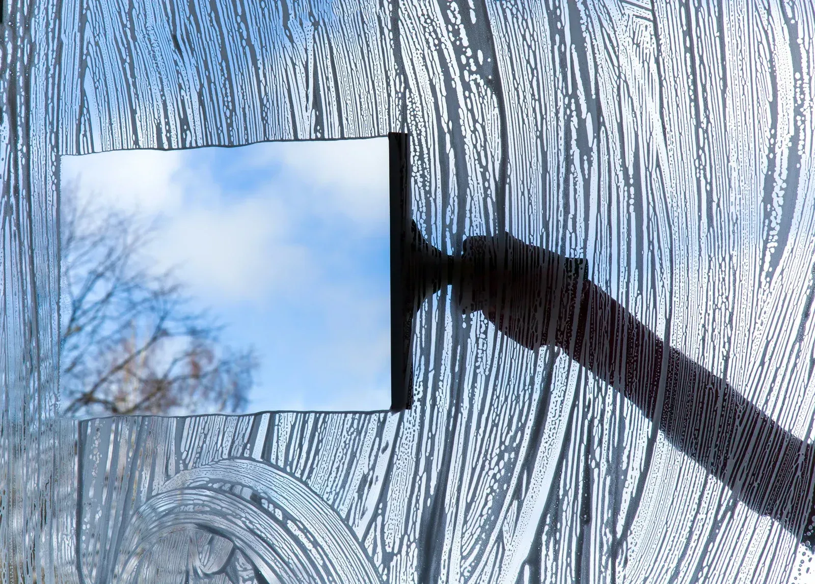 A person is cleaning a window with a squeegee and a mirror.