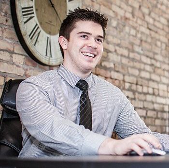 A man is sitting at a desk in front of a clock.