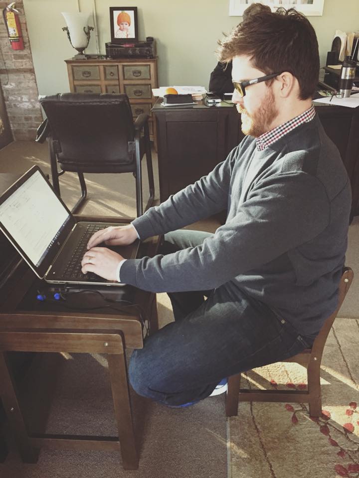 A man is typing on a laptop while sitting in a chair