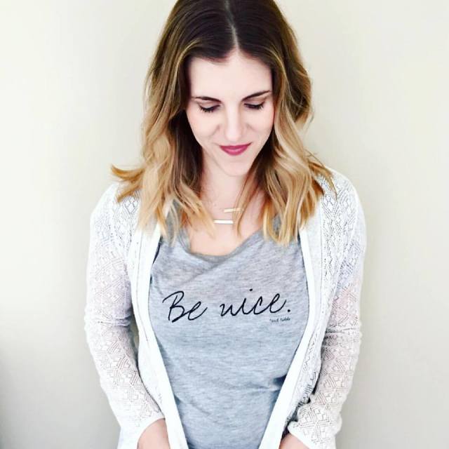 A woman is wearing a t-shirt that says `` be nice ''.