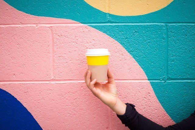 A person is holding a cup of coffee in front of a colorful wall.