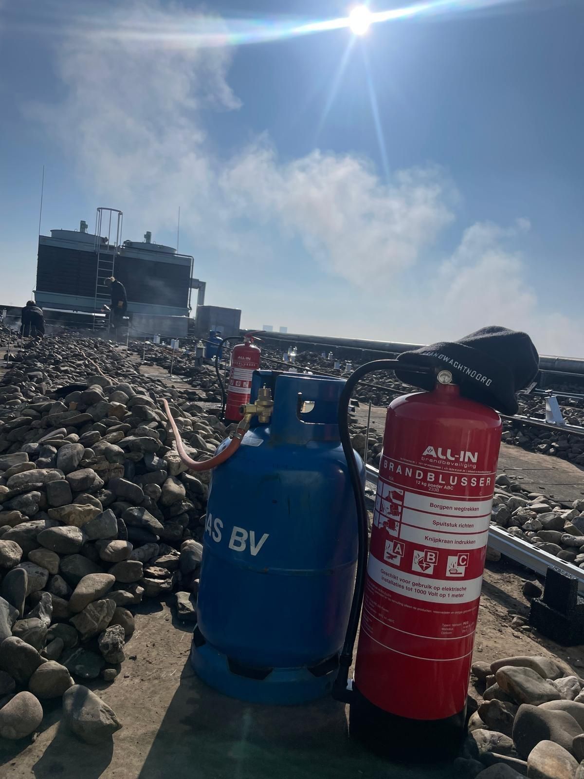 Een rode brandblusser en een blauwe gasfles staan ​​op een rotsachtige ondergrond in de felle zon.