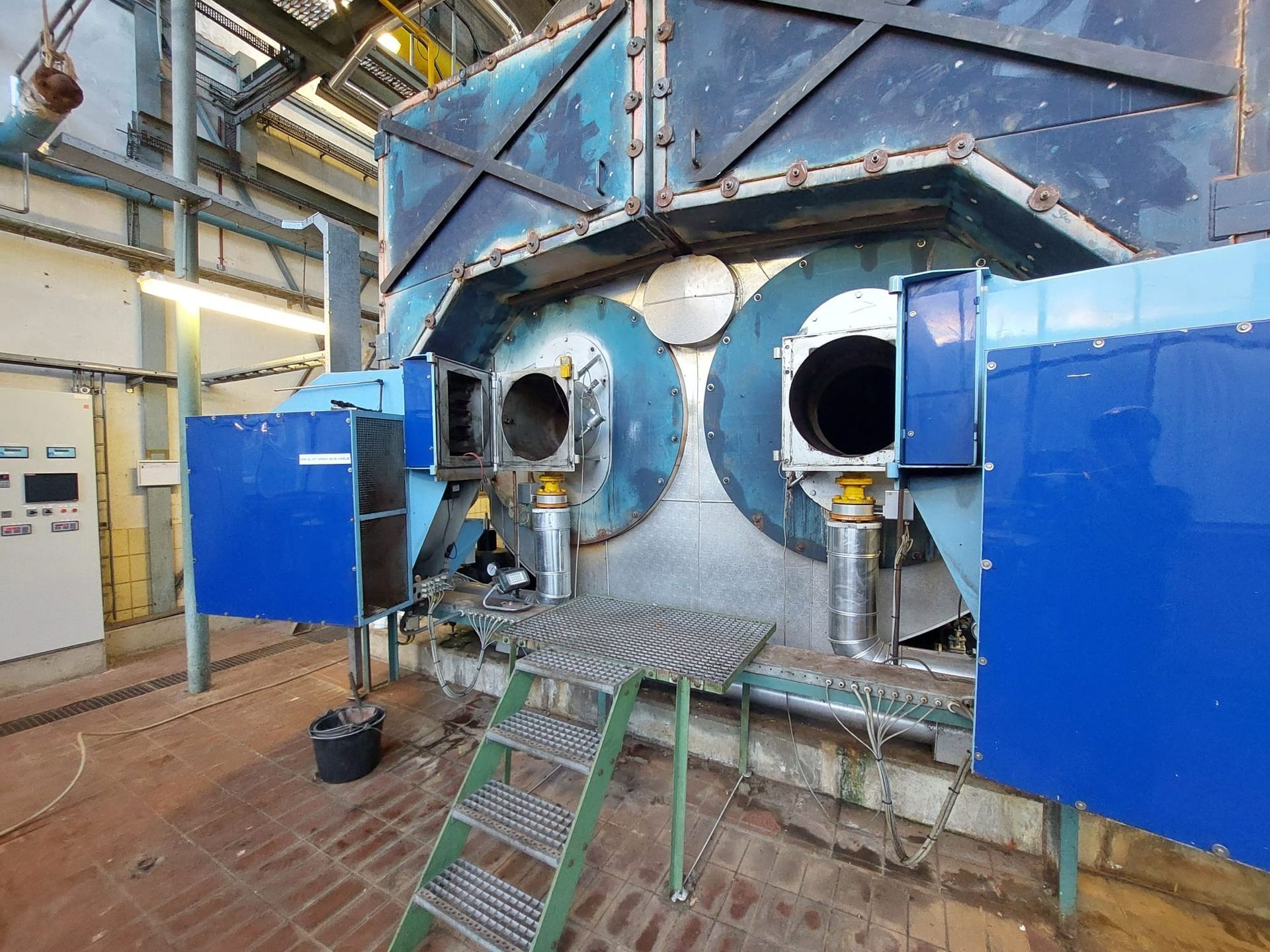 Twee grote, ronde industriële branders gemonteerd op een metalen machineframe in een binnenruimte met een metalen trap.