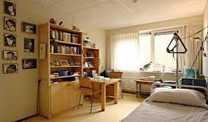 Een slaapkamer met een bed, bureau, boekenplank en schilderijen aan de muur.