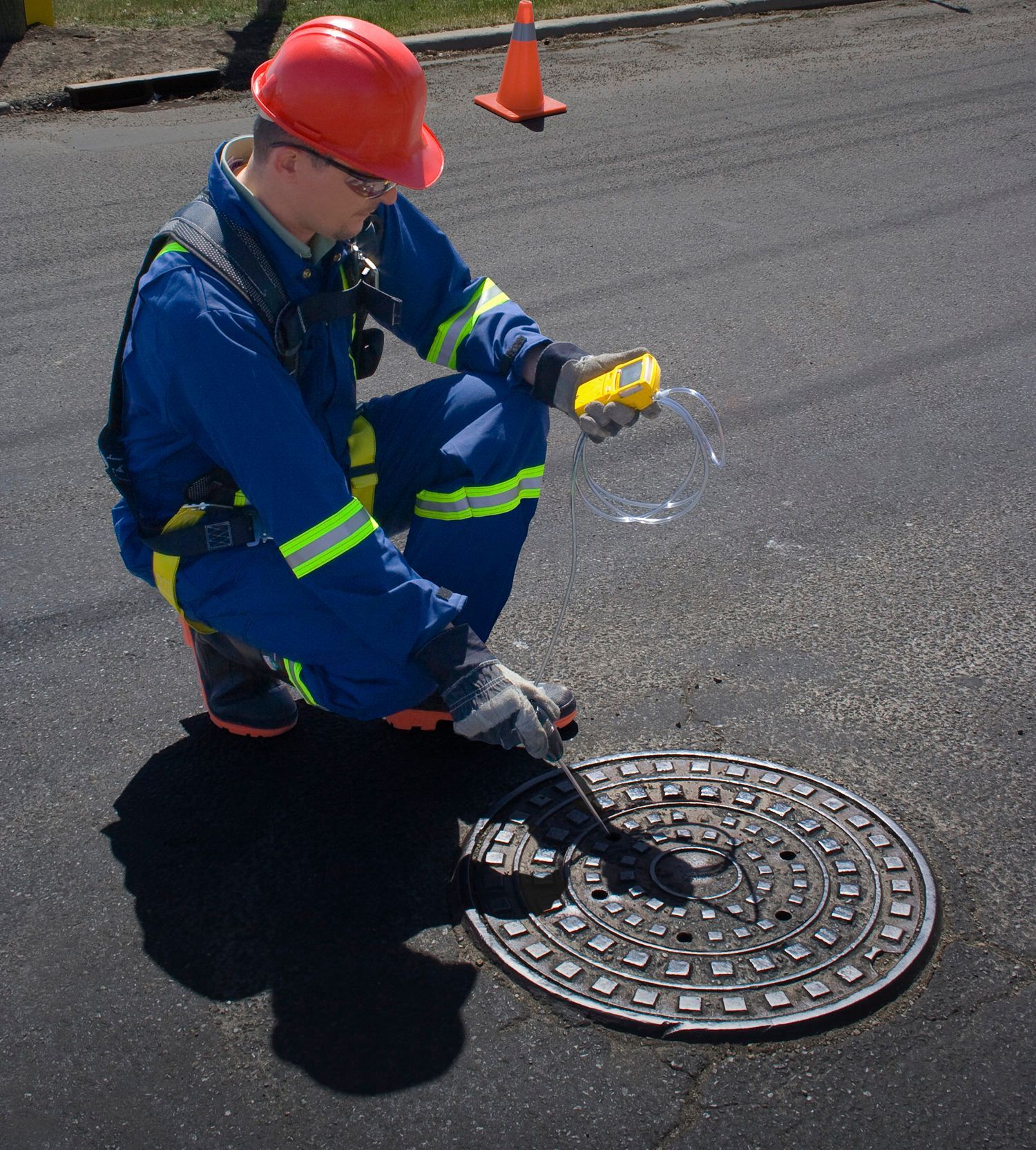 Een werknemer in veiligheidsuitrusting gebruikt een 4- gasmeter om H2S in de buurt van een putdeksel te meten.