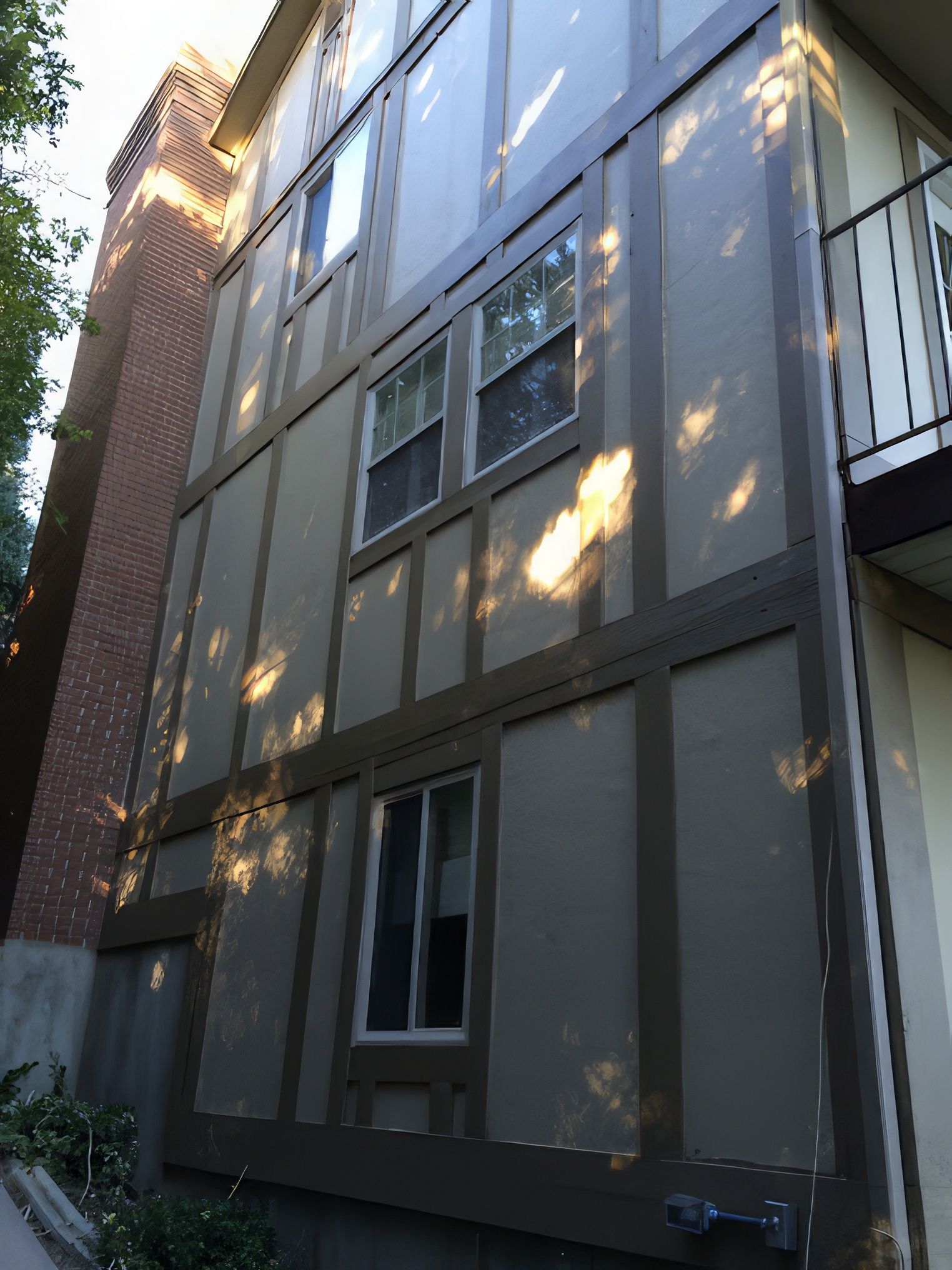 Two-story building exterior with dark trim and beige siding, windows, and a brick chimney.
