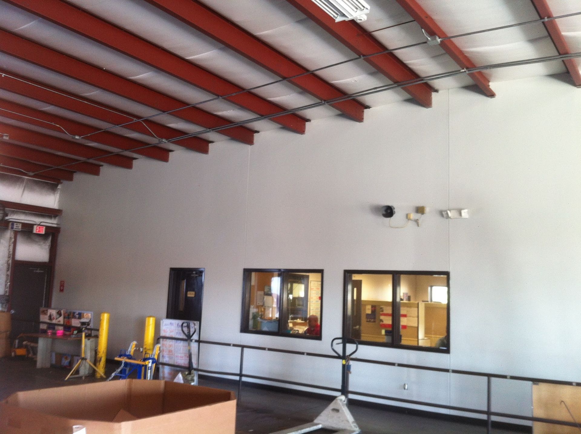 Interior view of a warehouse with exposed red beams, white walls, two windows, and boxes on the floor.